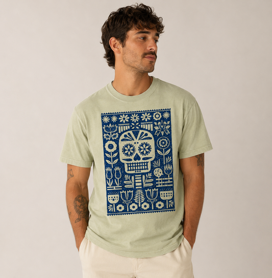 Man wearing a light green t-shirt with a blue and white skull design on a plain background
