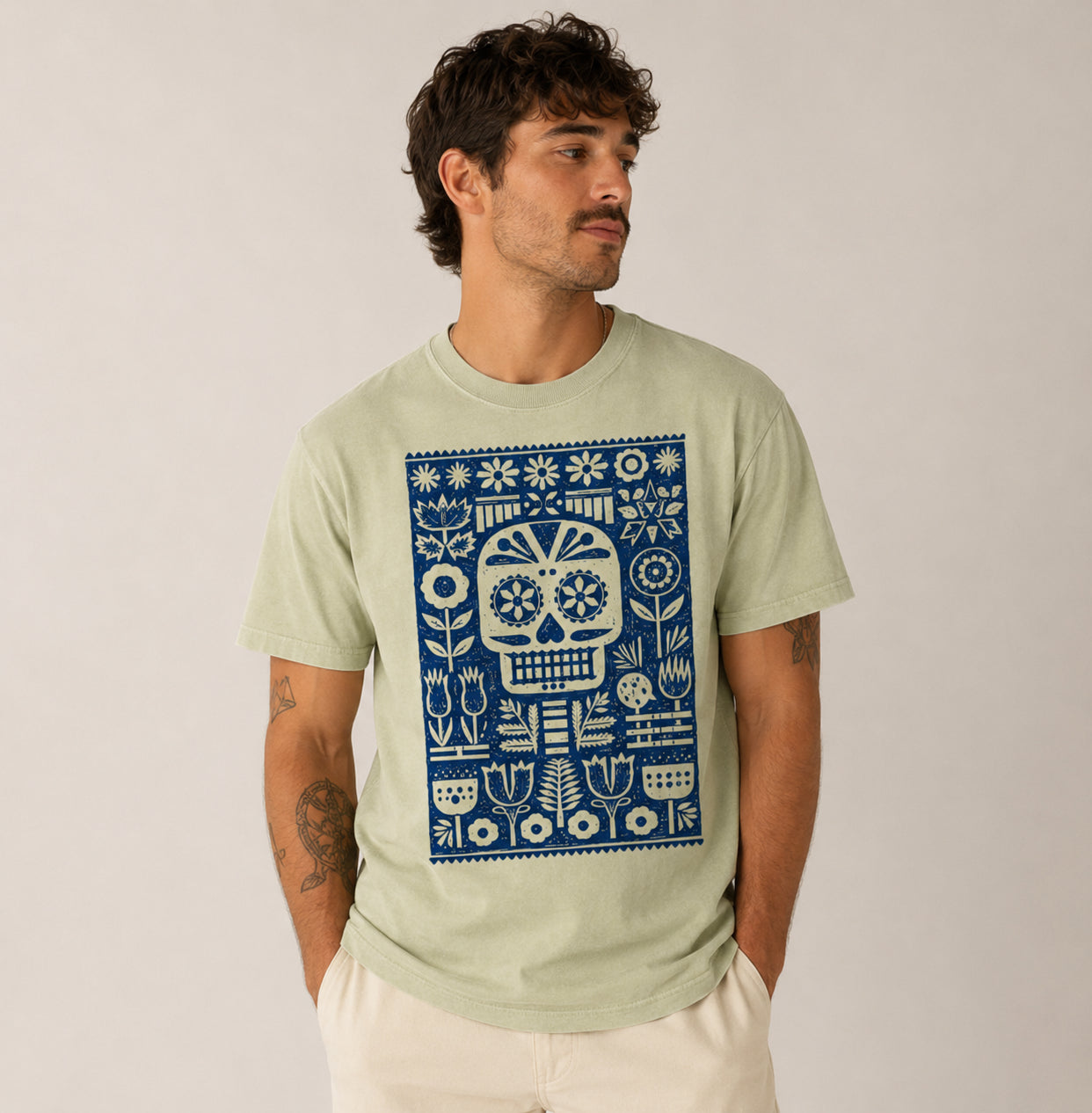 Man wearing a light greenFolk Skull graphic t-shirt featuring decorative skull artwork inspired by folk art and vintage illustration.