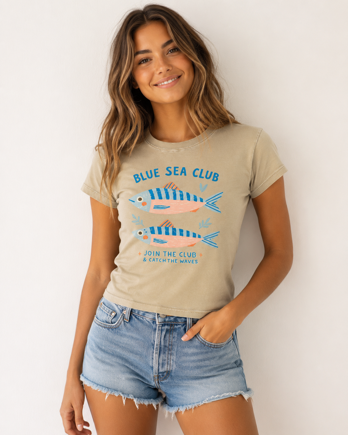 Woman wearing a beige Blue Sea Club graphic t-shirt featuring coastal-inspired artwork celebrating ocean adventures and seaside living.