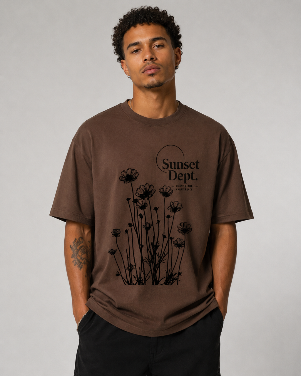 Man wearing a brown t-shirt with black floral design and 'Sunset Dept.' text on a gray background