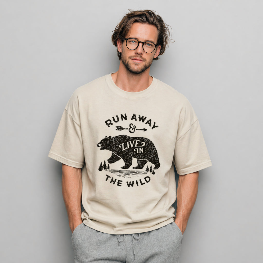 Man wearing a beige Run Away and Live in the Wild graphic t-shirt featuring bear artwork inspired by wilderness, nature, and outdoor adventure.
